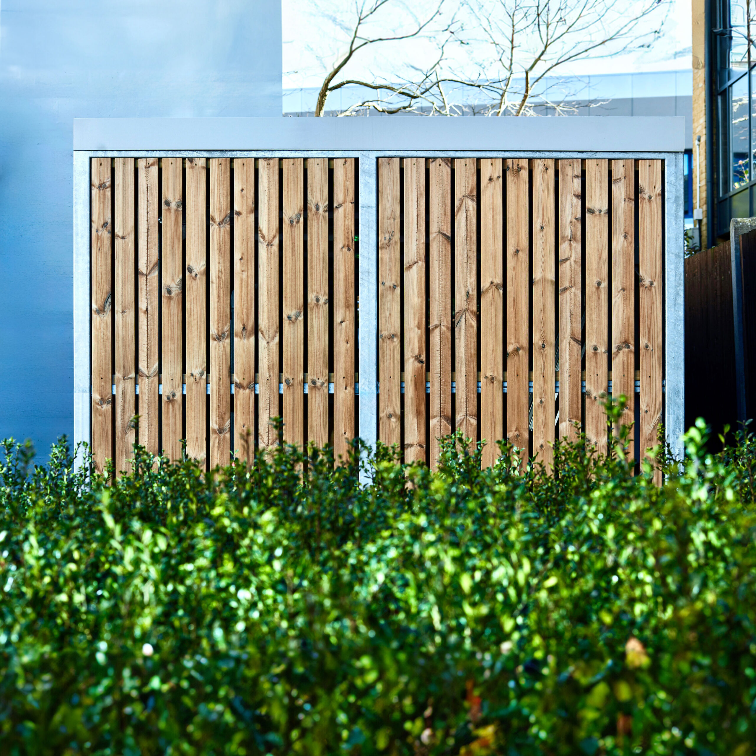 Amazon Semi Vertical Cycle Shelter with Timber Cladding infront of a bush installed outside of a commercial building